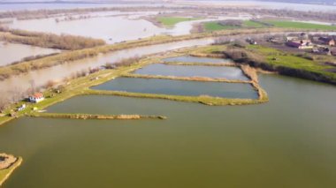 Bir kanalın yanındaki balık göletinin havadan görünüşü ve kırsal kesimde bahar mevsiminde sular altında kalan tarlalar.