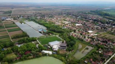 Sırbistan 'da Bulutlu Bahar Gününde Büyük Balık Havuzu ile Geniş Tarım Tarlaları Arasında Yerleşik Köy Manzarası