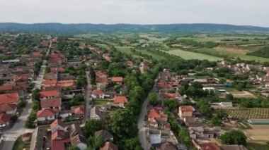 Bulutlu kış gününde tarımsal tarlaları olan bir köyün, arka planda duran tepelerin hava görüntüleri.
