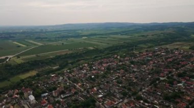 Bulutlu kış gününde tarımsal tarlaları olan bir köyün, arka planda duran tepelerin hava görüntüleri.