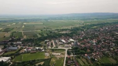 Bulutlu kış gününde tarımsal tarlaları olan bir köyün, arka planda duran tepelerin hava görüntüleri.