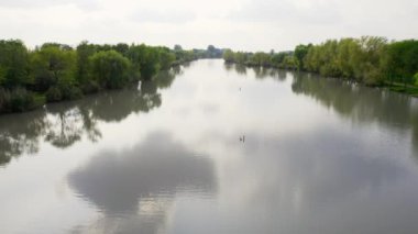 Hava aracı bulutlu bir sonbahar gününde gölün yüzeyinde uçuyor, Sırbistan 'da gölü saran yemyeşil ağaçlar ve çalılar