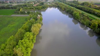 Bir gölü çevreleyen geniş yeşil alan, köye doğru uçan insansız hava aracı, Sırbistan 'da bulutlu Ekim günü