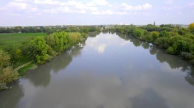 Hava aracı bulutlu bir sonbahar gününde gölün yüzeyinde uçuyor, Sırbistan 'da gölü saran yemyeşil ağaçlar ve çalılar