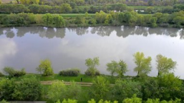 Hava aracı bulutlu bir sonbahar gününde gölün yüzeyinde uçuyor, Sırbistan 'da gölü saran yemyeşil ağaçlar ve çalılar