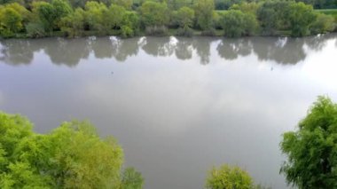 Hava aracı bulutlu bir sonbahar gününde gölün yüzeyinde uçuyor, Sırbistan 'da gölü saran yemyeşil ağaçlar ve çalılar