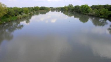 Hava aracı bulutlu bir sonbahar gününde gölün yüzeyinde uçuyor, Sırbistan 'da gölü saran yemyeşil ağaçlar ve çalılar