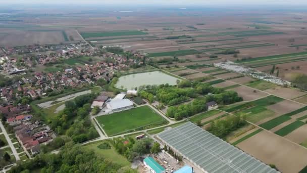 セルビアのセルビアで大きな魚の池を持つ広大な農業分野に位置する村の空中ビュー — ストック動画