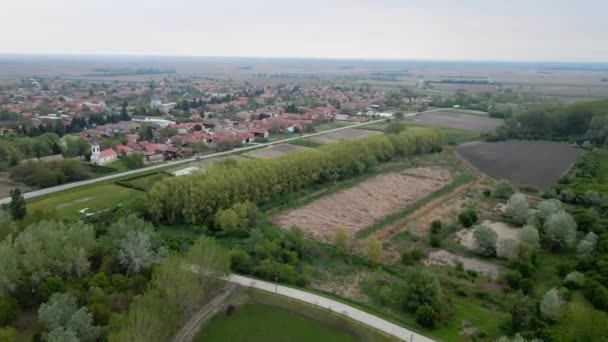 セルビアの雲の春の日に広がる農業分野に位置するビレッジの空中ビュー — ストック動画