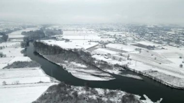 Kasvetli bir günde karla kaplı şehrin içinden akan bir nehrin havadan görünüşü.