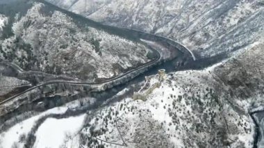 Karla kaplı dağların tepesinde ortaçağdan kalma bir şatonun bulunduğu havadan bir kış manzarası.
