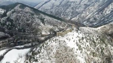 Karla kaplı dağların tepesinde ortaçağdan kalma bir şatonun bulunduğu havadan bir kış manzarası.