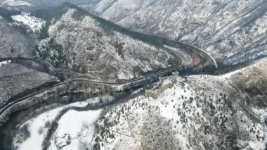 Karla kaplı dağların tepesinde ortaçağdan kalma bir şatonun bulunduğu havadan bir kış manzarası.