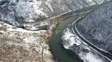 Drone kış günü dağların eteklerinde nehre doğru uçuyor.
