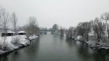 Nehir yüzeyinden bir uçuş, kış manzarasında bir köprüye doğru gidiyor.