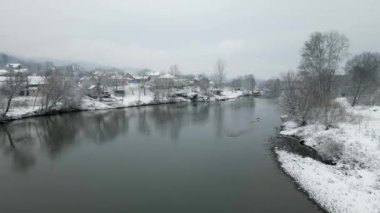 Bulutlu bir kış gününde, karla kaplı bir nehrin drone çekimi.