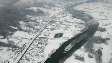 Karla kaplı kırsal bir arazinin havadan görünüşü, kasabada dolaşan bir nehir.
