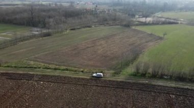 Köye doğru tarımsal tarlalarla çevrili toprak yolda giden arabanın insansız hava aracı görüntüsü.