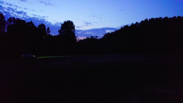 美丽的无人驾驶飞机拍摄了小镇上空的一个夜晚和一辆开着灯的汽车 — 图库视频影像