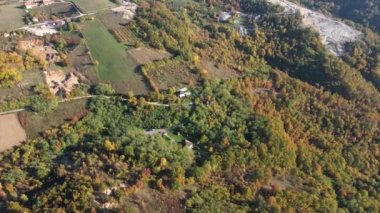 Güneşli sonbahar gününde küçük evler etrafa saçılmış ağaçlık alan manzarası.