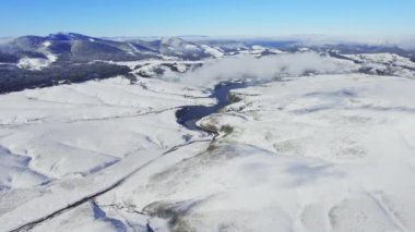 Donmuş göl karla kaplı kara bulutlardan görünen dağlarla çevrili.