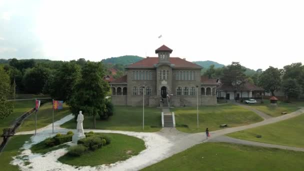 一架无人驾驶飞机拍摄到一座历史性建筑的照片 这所建筑是一所小学 顶部装饰着塞尔维亚国旗 在前景展望中 难以辨认的孩子们正坐在那里 — 图库视频影像
