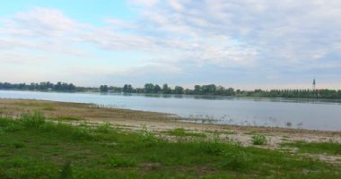 Nehrin karşısından kumlu ve otlarla kaplı bir plajda duran şehir manzarasını görüntüler.