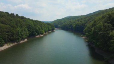 Tanımlanamayan üç avcı çayırdaki geyiklere doğru yürüyor. Etrafı orman ve dağlarla çevrili.