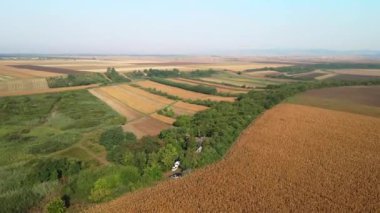 Mavi gökyüzünün altında ekili tarlaları ve ormanları olan kırsal bölge yukarıdan görünüyor.