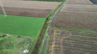 Floresan giysili bir grup adam, insansız hava araçlarıyla toprak yolda yürüyorlar.