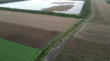 İnsanlar toprak yolda yürürken, göl ve tarlaları olan kırsal alan manzarası.