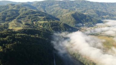 İnsansız hava aracı kasabanın yukarısında yeşil ağaçlık tepelerde duman yakalıyor.