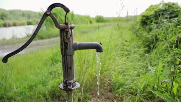 草の湖の近くに立っている深い井戸の蛇口から注ぐ水 — ストック動画