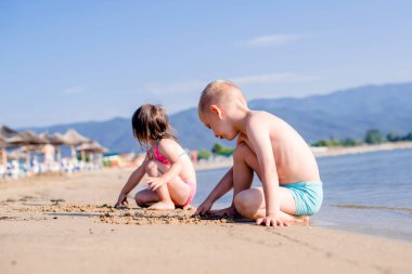 Çocuklar kumsalda kumda resim çiziyor.