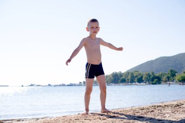 Arkasında denizle sahilde duran bir çocuk.