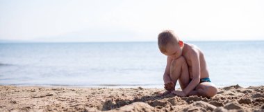 Küçük sarışın çocuk kumsalda oynuyor.