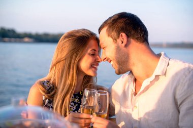 Genç bir çift teknede eğleniyor, şampanya içiyor ve gülümsüyor.