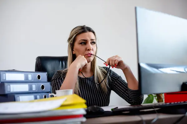 Endişeli Sekreter ofisteki bilgisayara bakıyor ve elinde gözlük tutuyor.