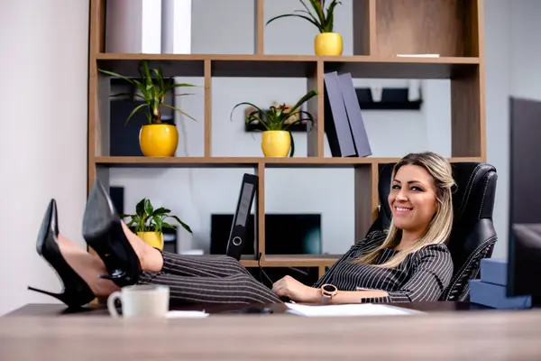 Ofisinde bacakları masanın üstünde oturan sarışın bir iş kadını.