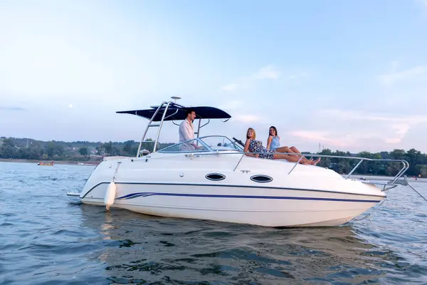 Genç bir adam ve iki kadın yaz günbatımında teknede eğleniyorlar.