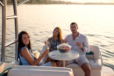 Genç bir adam ve iki güzel kadın teknede eğleniyor, yaz günbatımında parti veriyorlar.