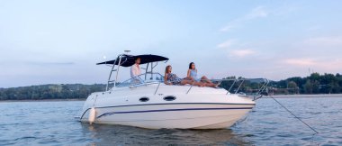 Genç bir adam ve iki kadın yaz günbatımında teknede eğleniyorlar.