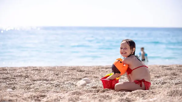 Şirin küçük kız güzel, çakıllı kumsalda oynuyor ve gülümsüyor.