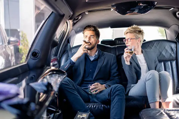 İş kadını ve iş adamı limuzinde içki içiyorlar.