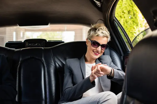 Limuzindeki iş kadını, gülümsüyor ve saatine bakıyor..