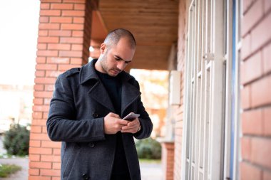 Güneşli şehir caddesinde cep telefonu kullanan bir işadamı, mesajlaşma üzerine yoğunlaşmış..