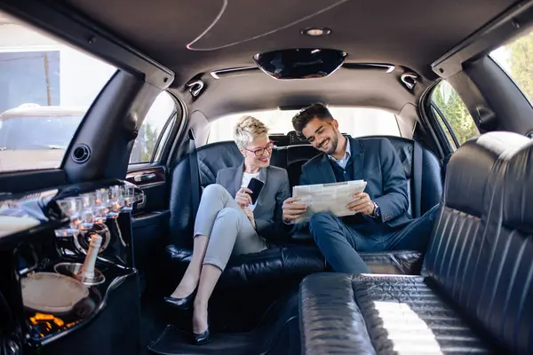 Partners in limo looking at newspaper, getting informed