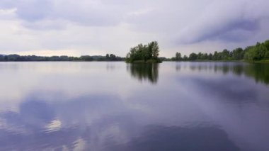 İnsansız hava aracı sakin gölün yüzeyinde ağaçlarla kaplı küçük bir adaya doğru uçar.