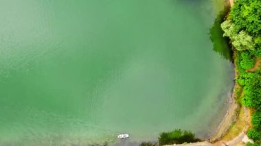 İnsansız hava aracı açık yeşil göl yüzeyine, üzerinde beyaz bir tekne ile iniyor.