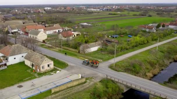 村を運転する乗客とカートを引くトラクターのドローンビデオ — ストック動画